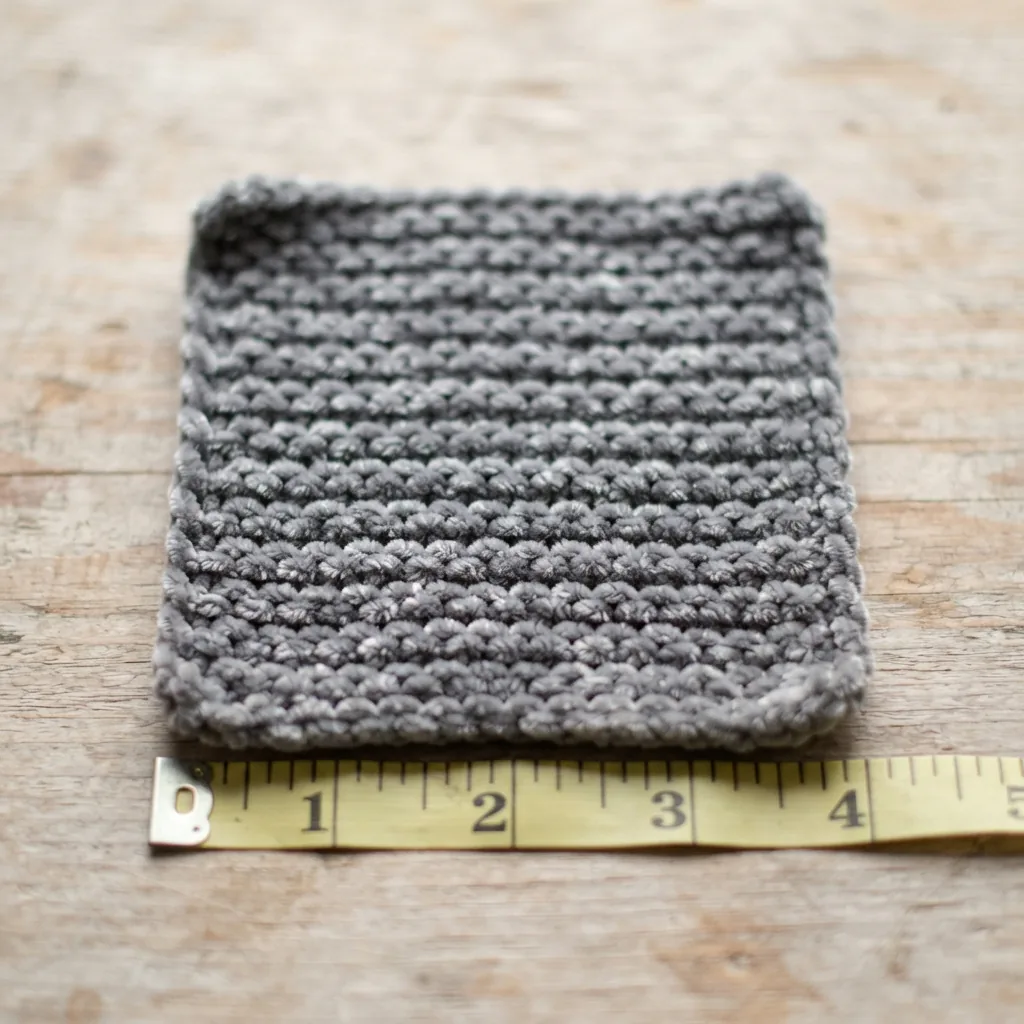 A knitted gauge swatch made from the chenille yarn next to a measuring tape.